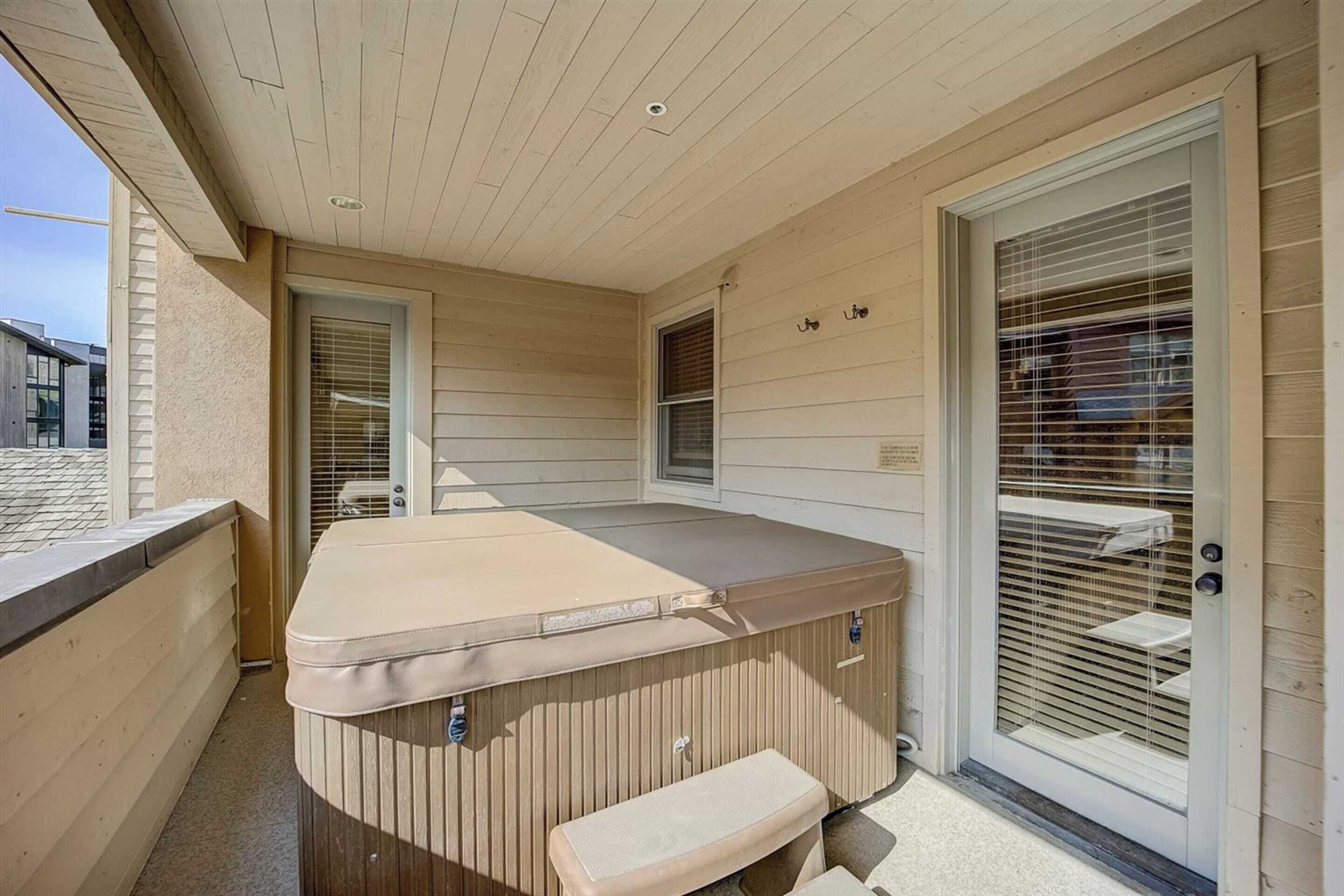 A hot tub with a bench, a door with a window, and a ceiling with wooden panels.