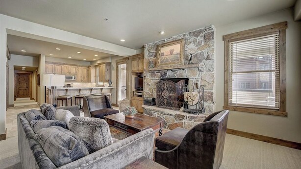 A spacious living room with a stone fireplace, a dining area with wooden cabinets, and a large window with blinds. - Mont Cervin by Avantstay Private Hot Tub + Fireplace Walk to Ski-in/ski-out + Dining (Park City)