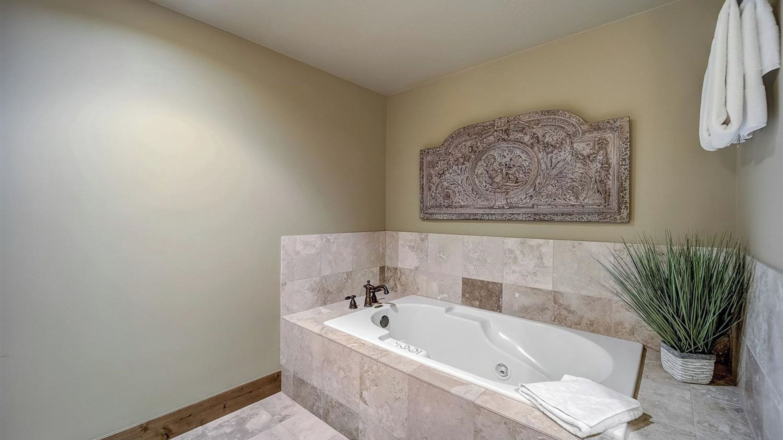 A bathroom with a freestanding bathtub, a decorative wall piece, and a potted plant.