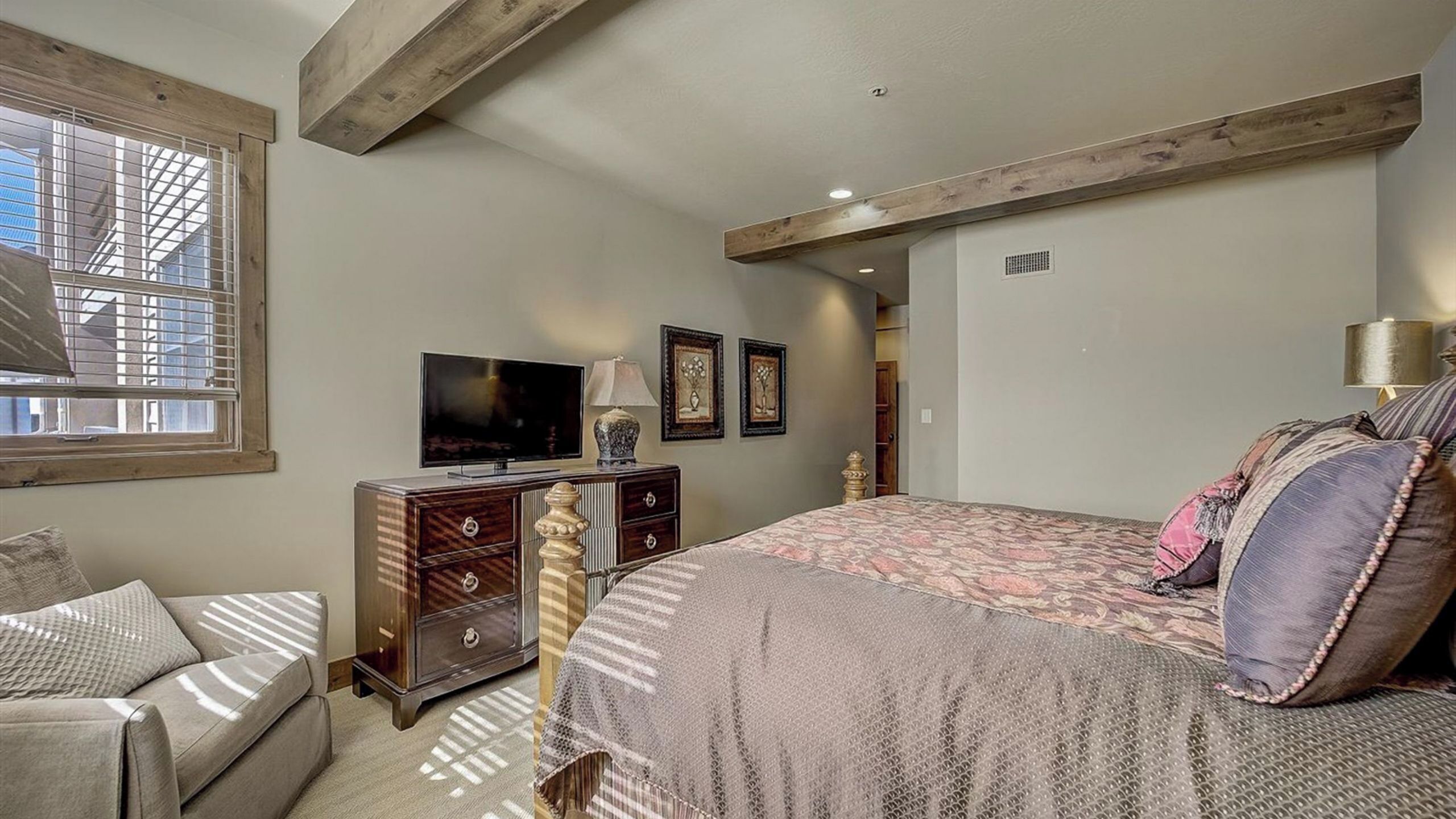A bedroom with a bed, a dresser, a television, and a window.