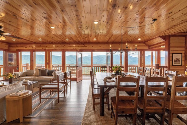 A wooden interior with a dining area, sofa, and large windows offering mountain views.