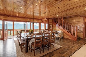 A wooden interior with a dining area, a staircase, and large windows.