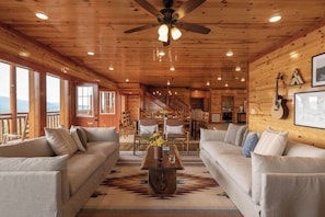 A spacious living area with a wooden ceiling, large windows, a staircase, and a dining area.
