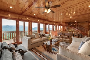 Relax in a spacious room with a high ceiling, sofa set, and dining area, offering a view of the surrounding landscape.