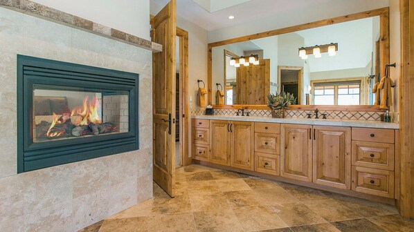 Un baño con chimenea, armarios de madera, un espejo grande y suelo de baldosas.