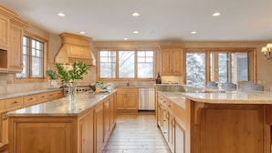 A spacious kitchen with wooden cabinets, a large island, and a view of snowy trees through the windows.