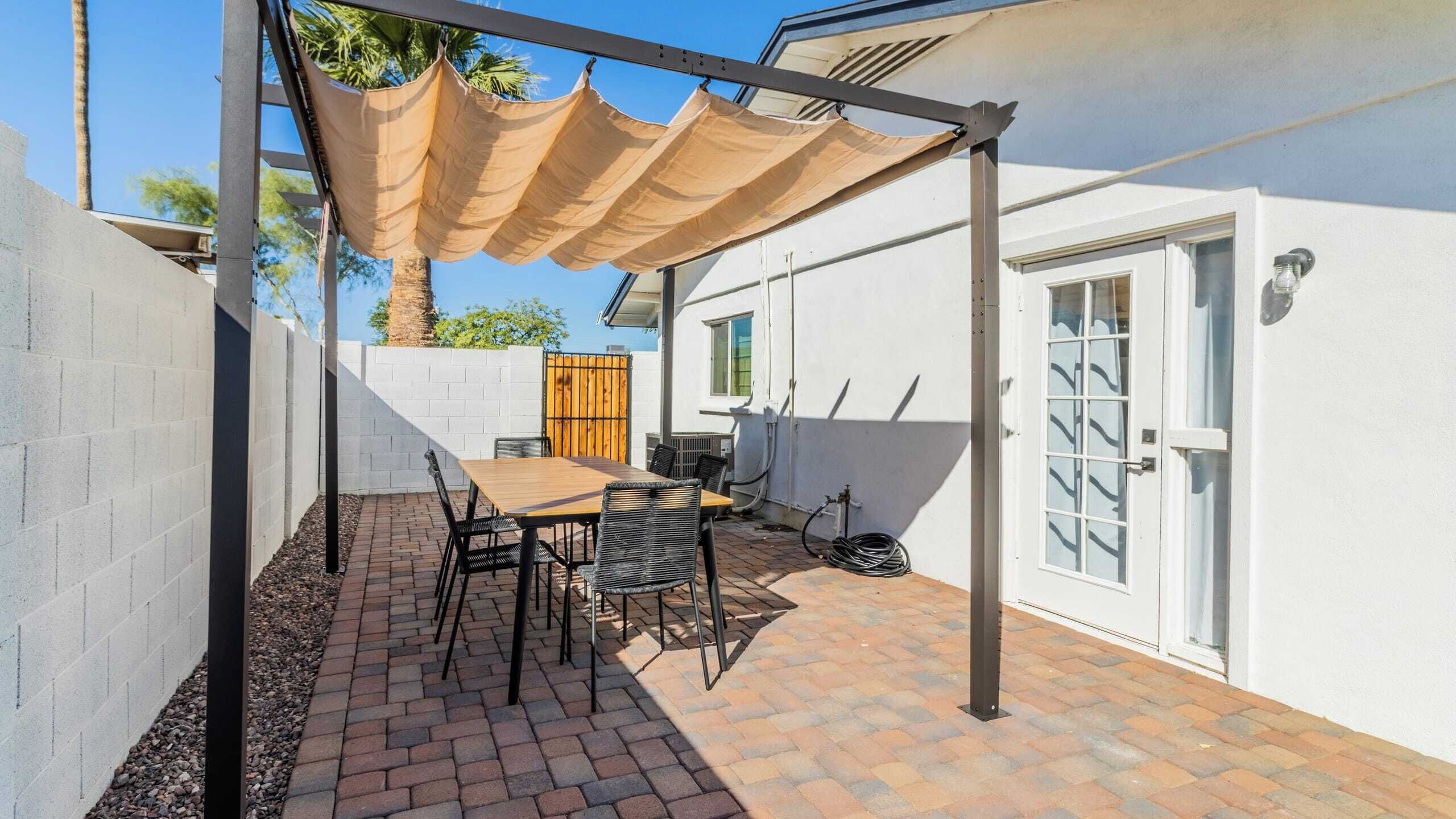 Une terrasse avec une table et des chaises, une pergola et un bâtiment blanc doté d’une porte et de fenêtres.