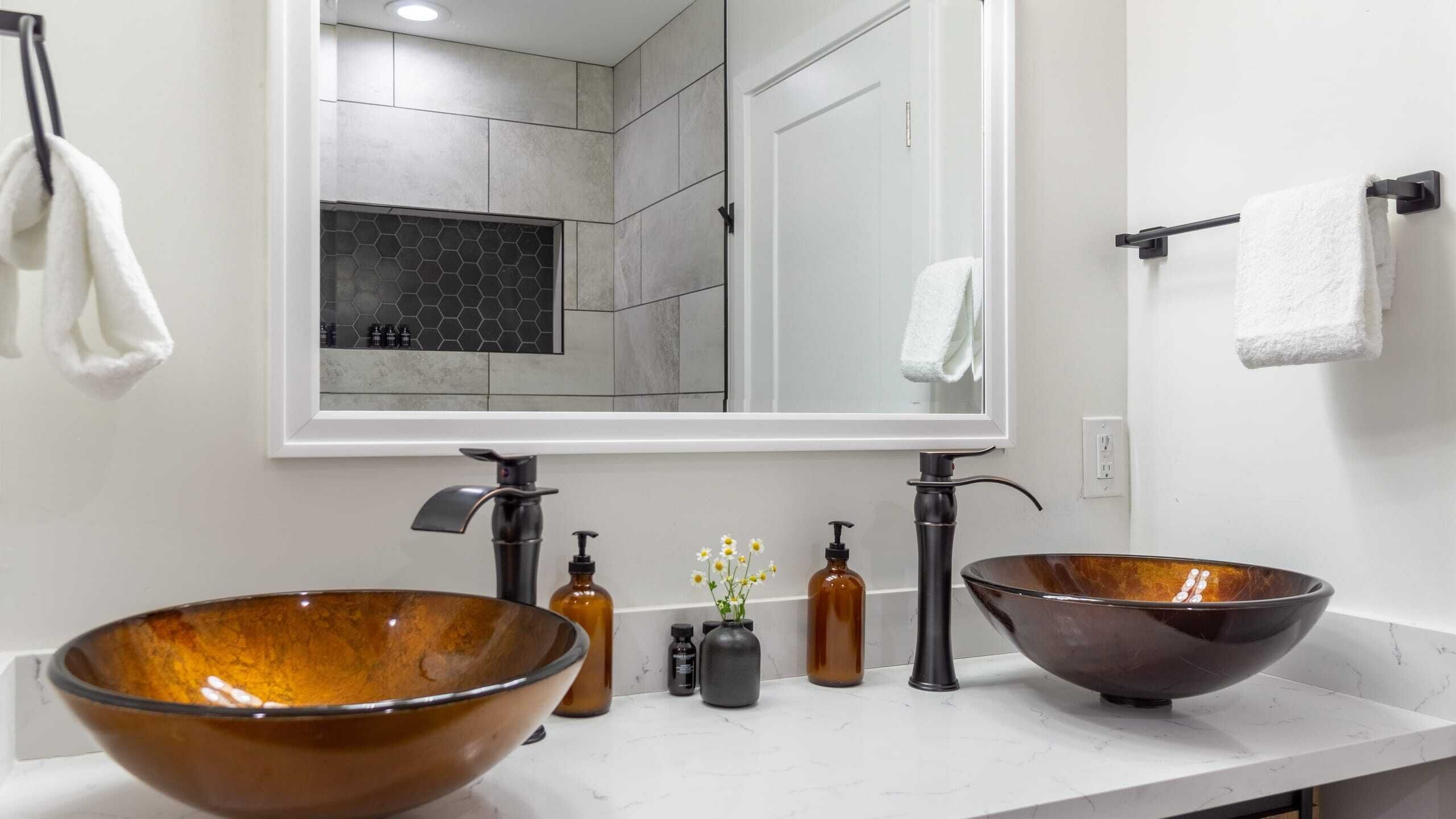 A bathroom with two large, brown, glossy bowls as sinks, a mirror above, and white towels hanging on hooks.