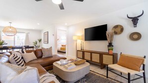 A modern living room with a brown leather sofa, a grey ottoman, and a wooden coffee table. There is a flat-screen TV mounted on the wall, a woven basket on a console table, and a decorative bull skull. - Rosario by Avantstay10mins to Old Town Scottsdale (Scottsdale)