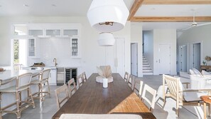 A spacious dining area with a long wooden table, white chairs, and a central decorative piece.