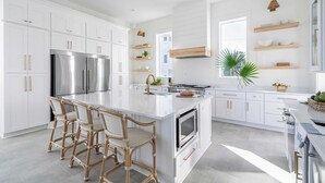 A modern kitchen with white cabinetry, stainless steel appliances, and a central island with bar stools. - Rendezvous by Avantstay Modern Haven w/ Game Room, Roof Top, Pool & Close to Beach! (Miramar Beach)