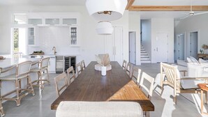 A spacious dining area with a wooden table, white chairs, and a central vase. - Rendezvous by Avantstay Modern Haven w/ Game Room, Roof Top, Pool & Close to Beach! (Miramar Beach)