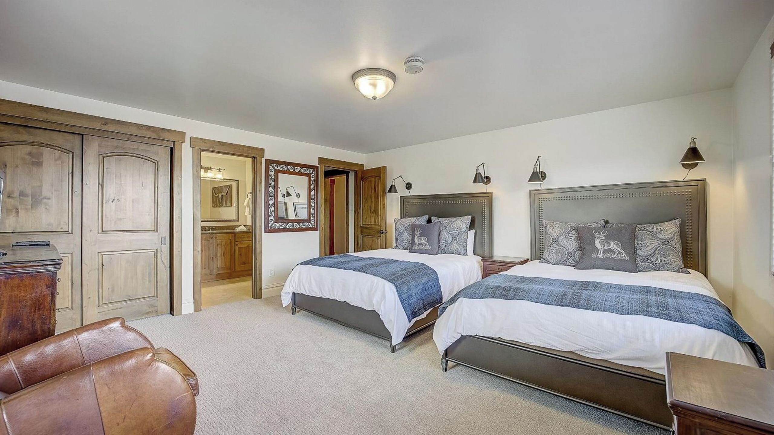A bedroom with two beds, a wooden wardrobe, a mirror, and a ceiling light.
