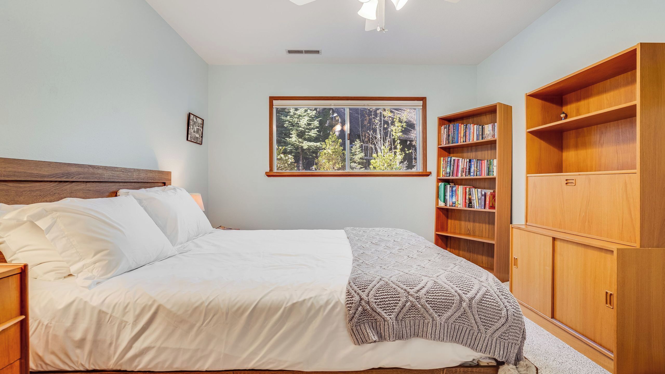 A bedroom with a bed, a window, a bookshelf, and a wardrobe.