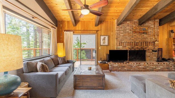 A cozy living room with a fireplace, a sofa, a television, and a ceiling fan.