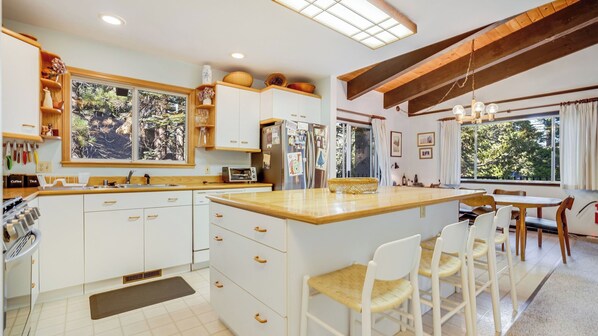 A modern kitchen with white cabinets, a large island, and a dining area with chairs. - Fawn by Avantstay Secluded Cabin w/ Large Deck Surrounded by Forest (Tahoma)