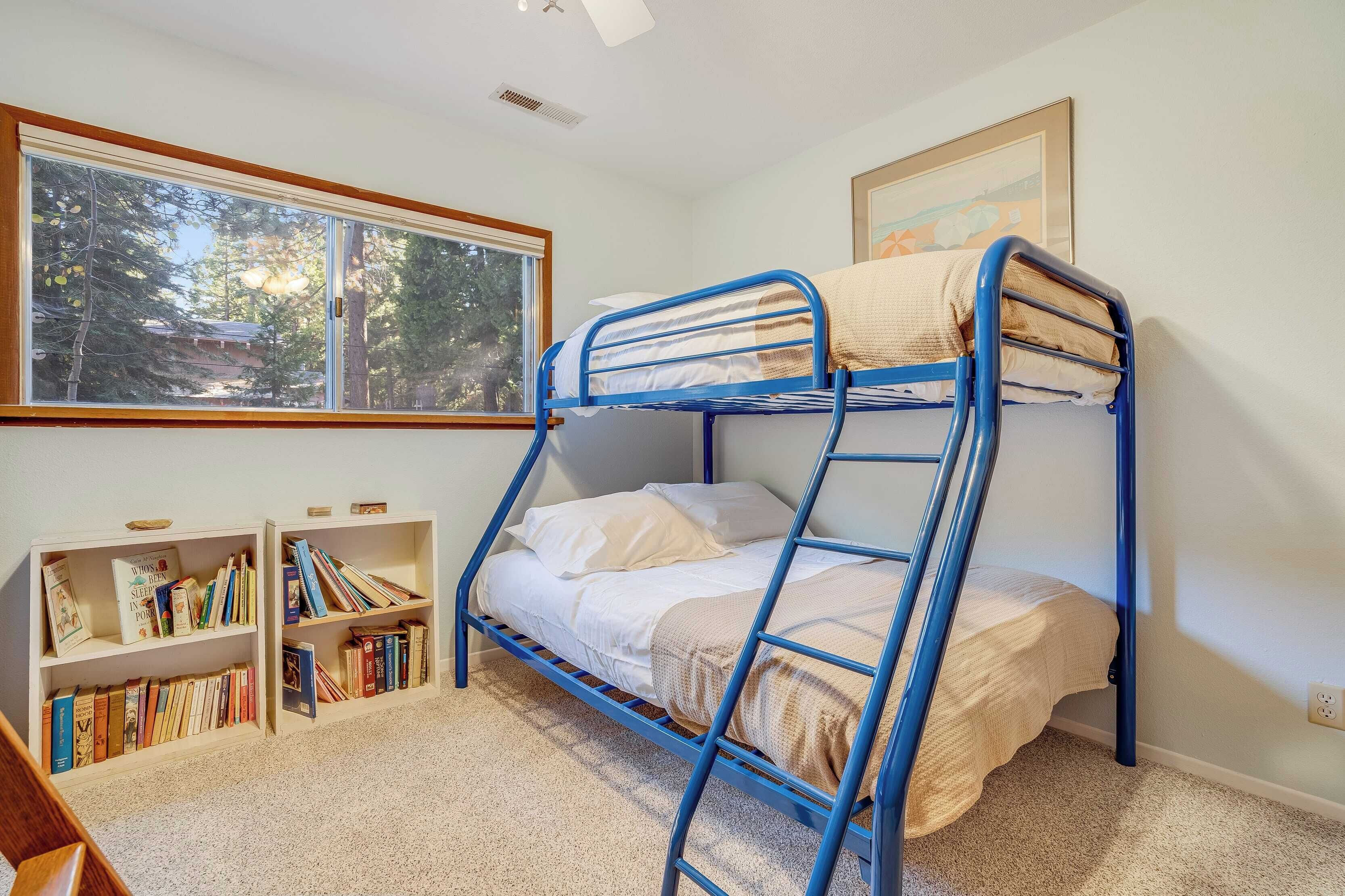 A bunk bed room with a large window, bookshelves, and a framed picture on the wall.