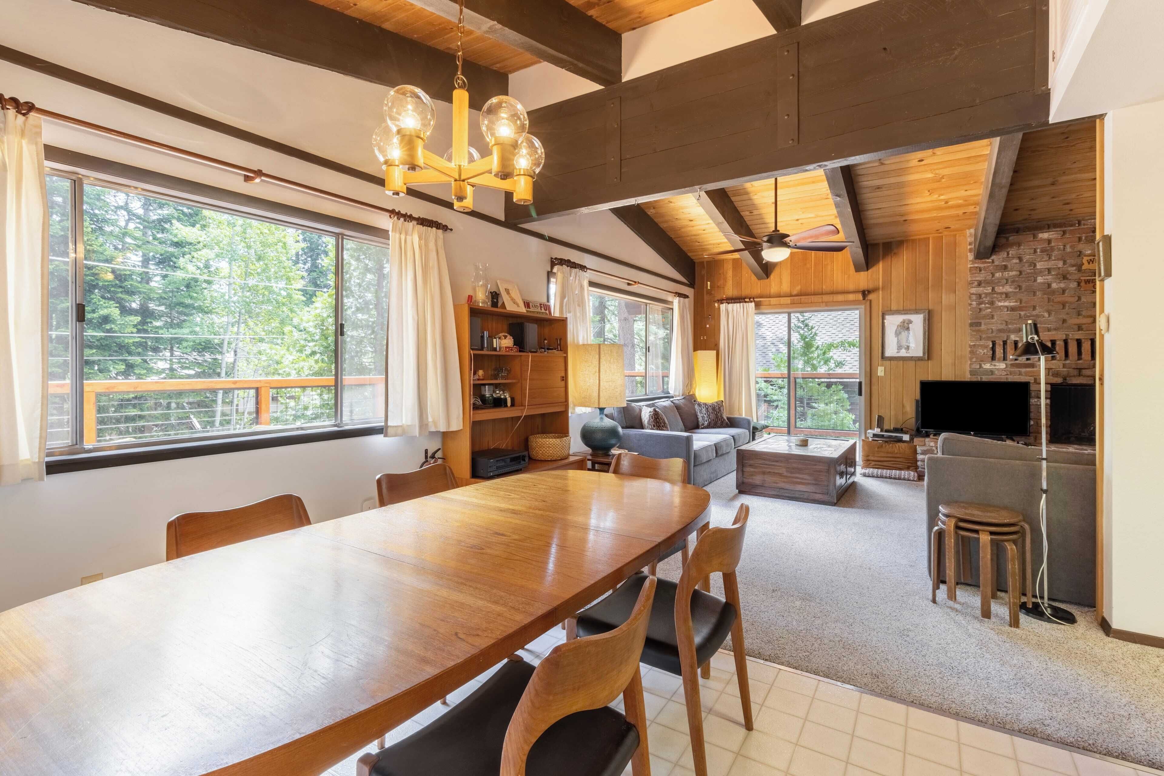 A spacious living area with a wooden dining table, comfortable seating, a fireplace, and large windows offering a view of the outdoors.