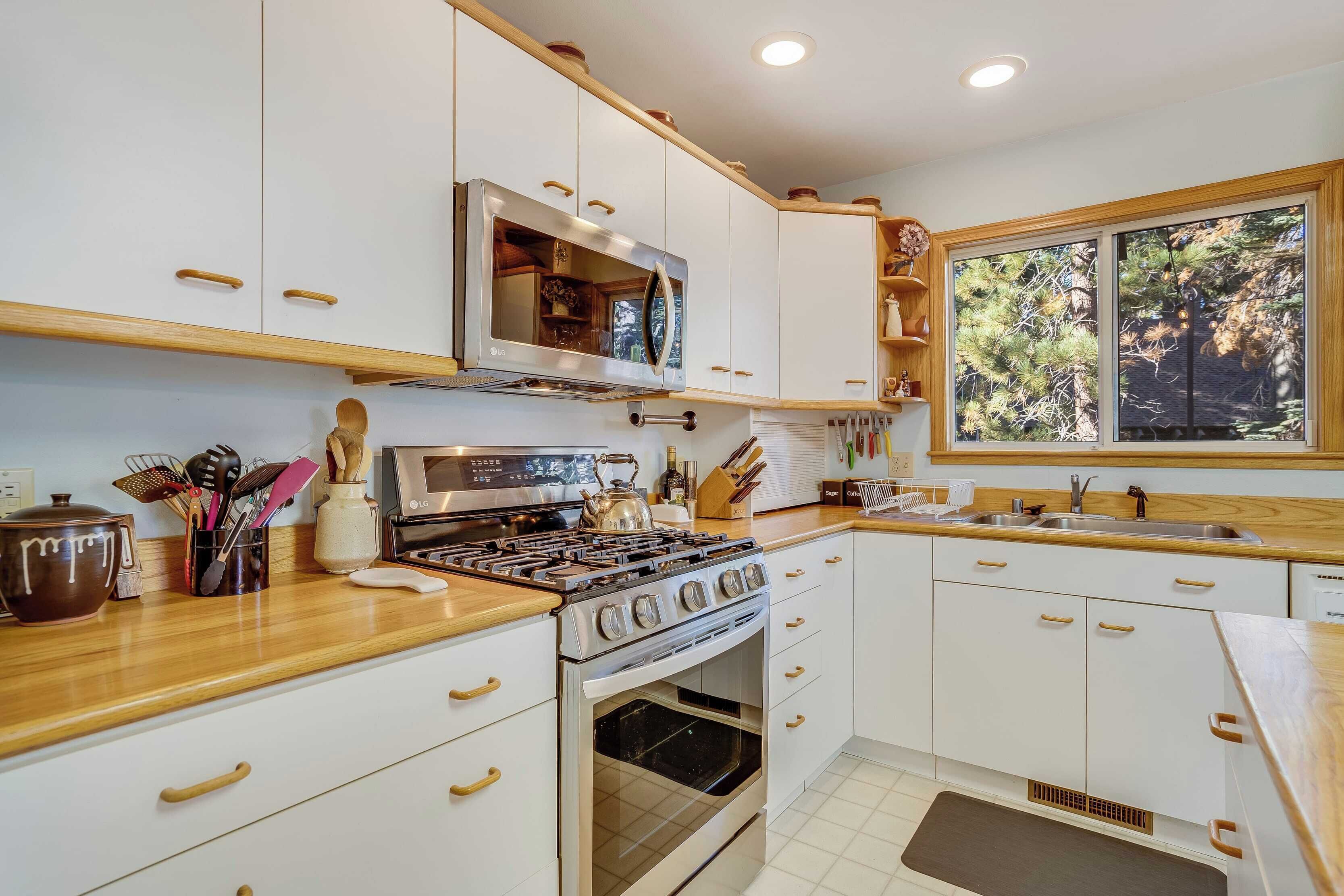 A modern kitchen with white cabinets, a stainless steel stove, and a microwave. There is a window providing natural light and a view of trees outside.