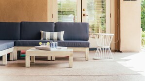 A modern living room with a dark blue sofa, a wooden coffee table, and a white side table. - Desert Grove by Avantstay Oasis Retreat w/ Pool & BBQ Grill! (Indio)