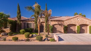 A residential house with a stone facade, multiple garage doors, and a well-maintained front yard with various shrubs and trees. - Desert Grove by Avantstay Oasis Retreat w/ Pool & BBQ Grill! (Indio)
