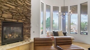 A cozy living room with a stone fireplace, leather chairs, a large window with a view, and a chandelier. - Arcadia by Avantstay Breathtaking Oasis in Scottsdale w/ Pool, Hot Tub & Game Room (Scottsdale)