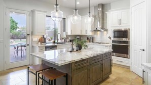 A modern kitchen with white cabinets, stainless steel appliances, and a large island with bar stools. - Arcadia by Avantstay Breathtaking Oasis in Scottsdale w/ Pool, Hot Tub & Game Room (Scottsdale)