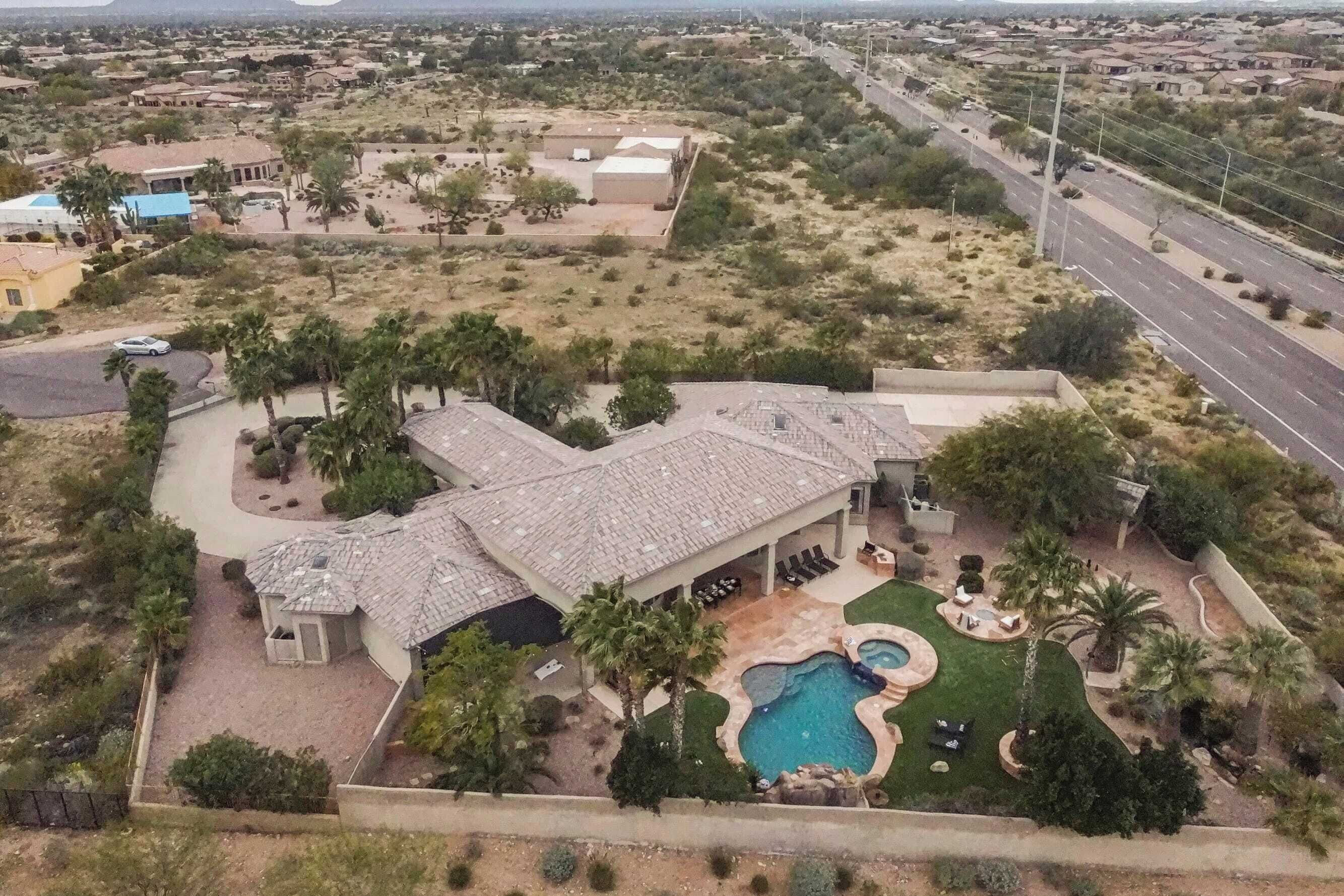 A large house with a swimming pool, surrounded by palm trees and a desert landscape.