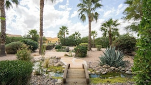 A garden with a wooden bridge, palm trees, and a small pond.