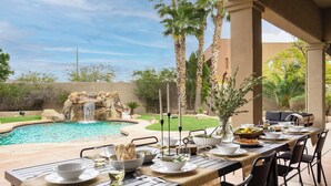 An outdoor dining area with a pool, waterfall, and palm trees. - Arcadia by Avantstay Breathtaking Oasis in Scottsdale w/ Pool, Hot Tub & Game Room (Scottsdale)