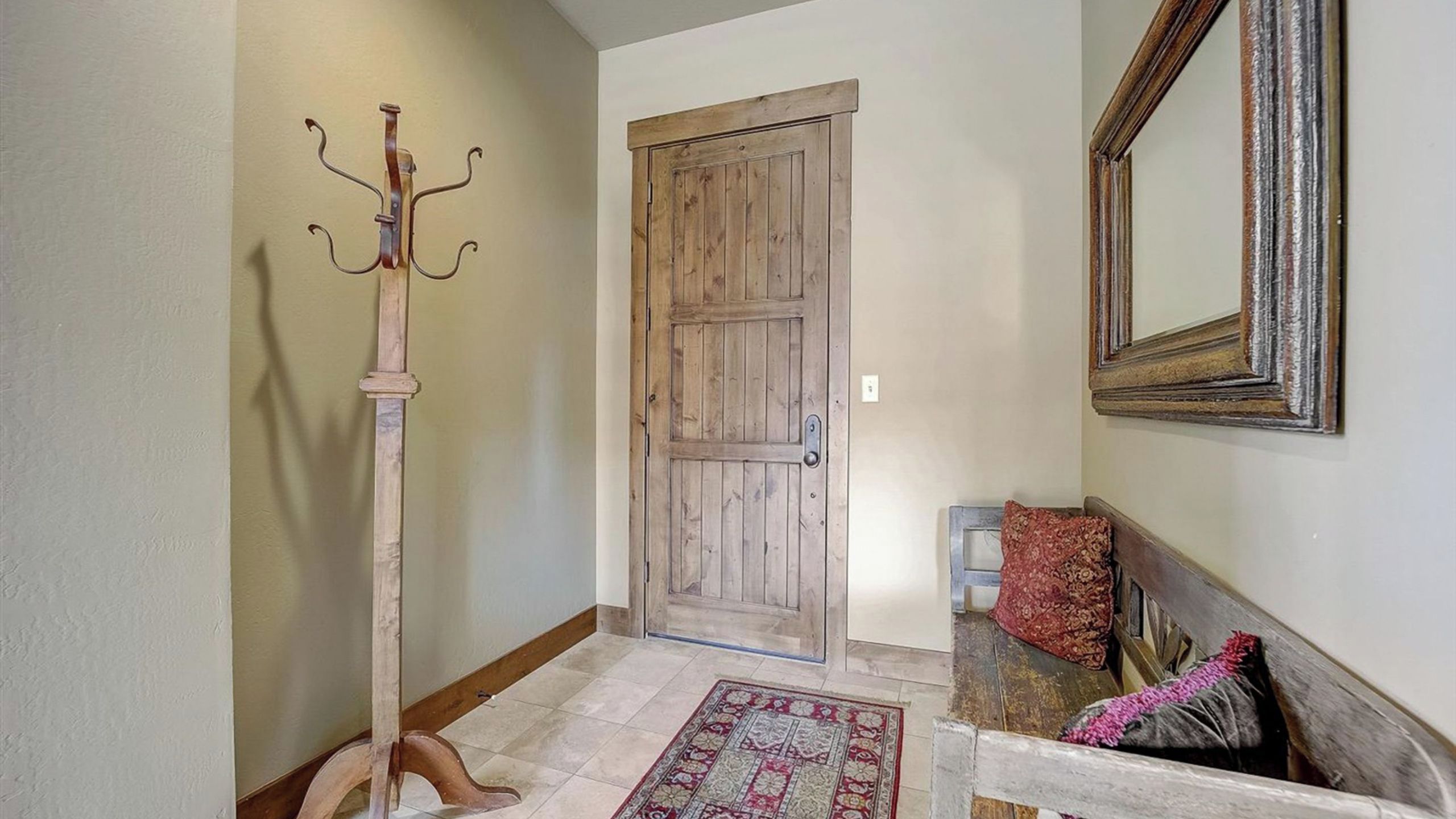 A hallway with a wooden door, a coat rack, a mirror, and a patterned rug.