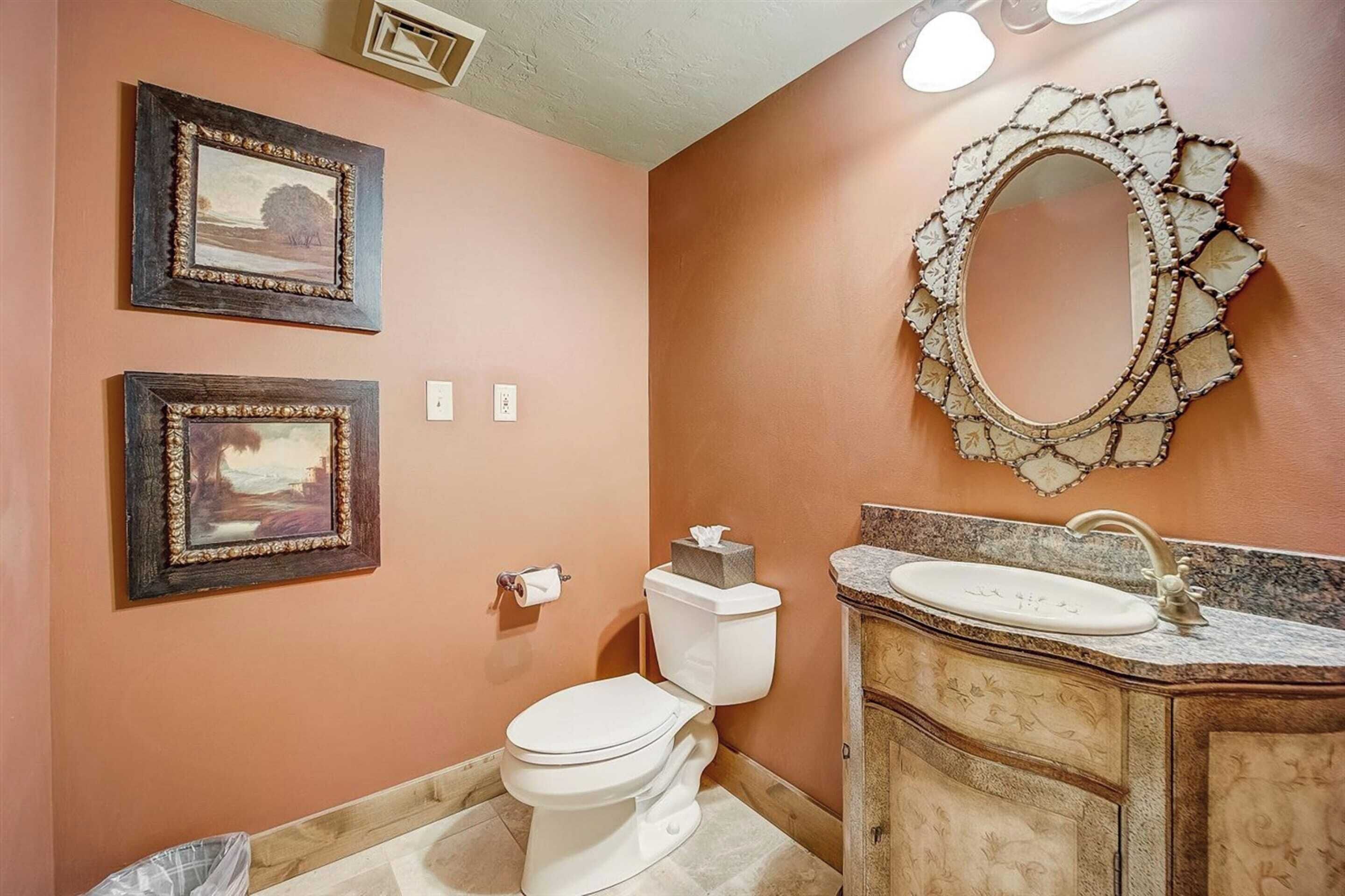 A bathroom with a toilet, sink, and two framed pictures on the wall.