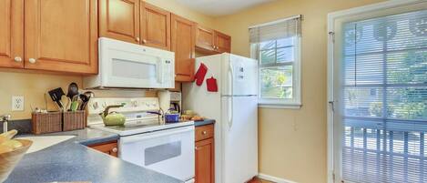 A kitchen with wooden cabinets, a white microwave, a stove, a refrigerator, and a window with blinds.