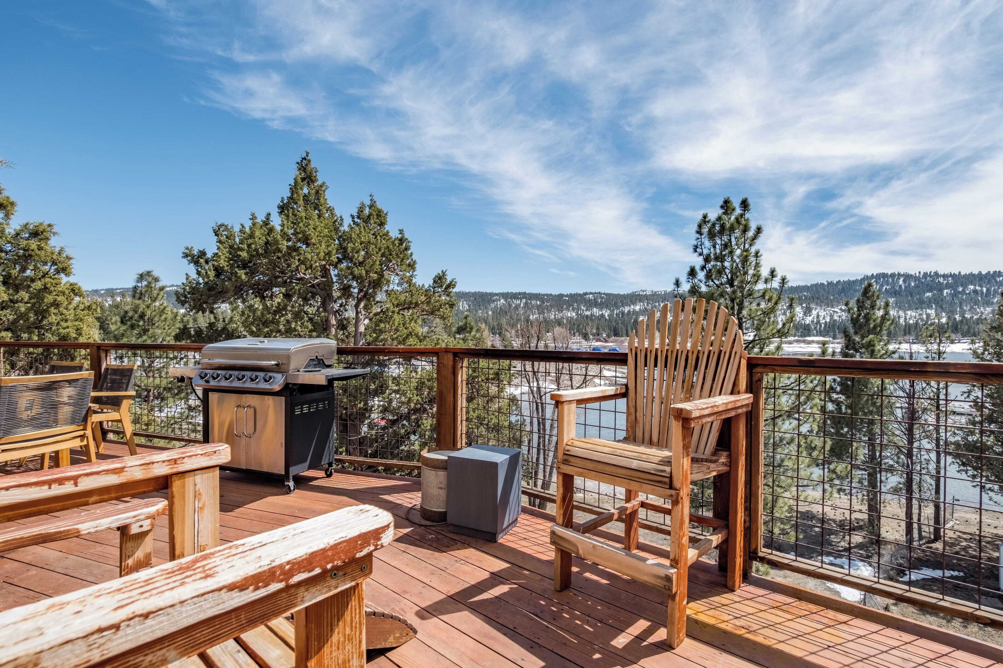 Une terrasse en bois avec un barbecue, des chaises et une vue sur une zone boisée.