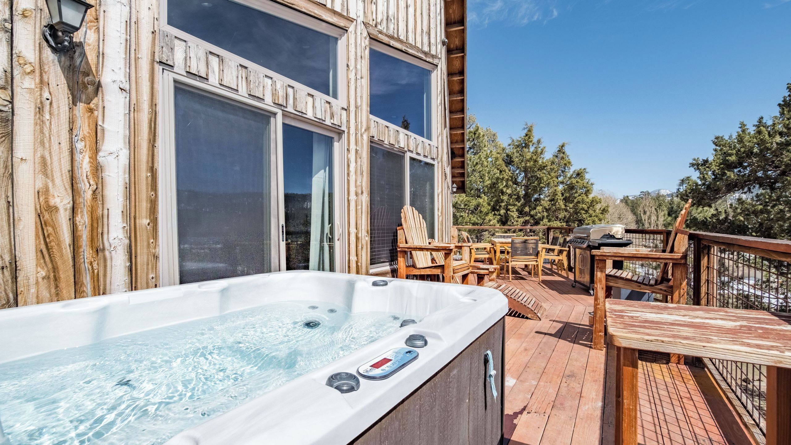 A hot tub on a wooden deck with outdoor furniture and a view of the surrounding landscape.