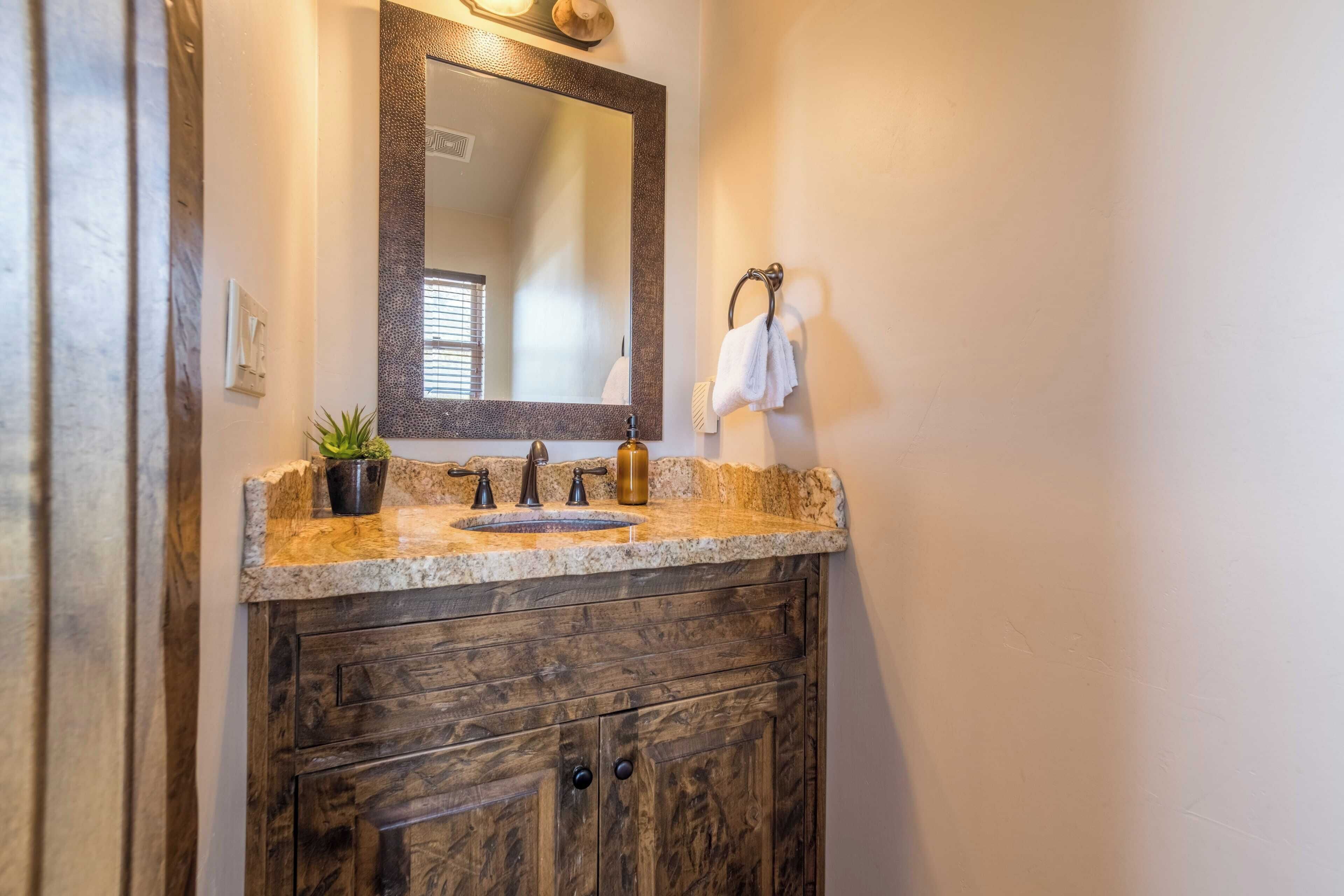 A bathroom with a granite countertop, a sink, a mirror, and wooden cabinets.