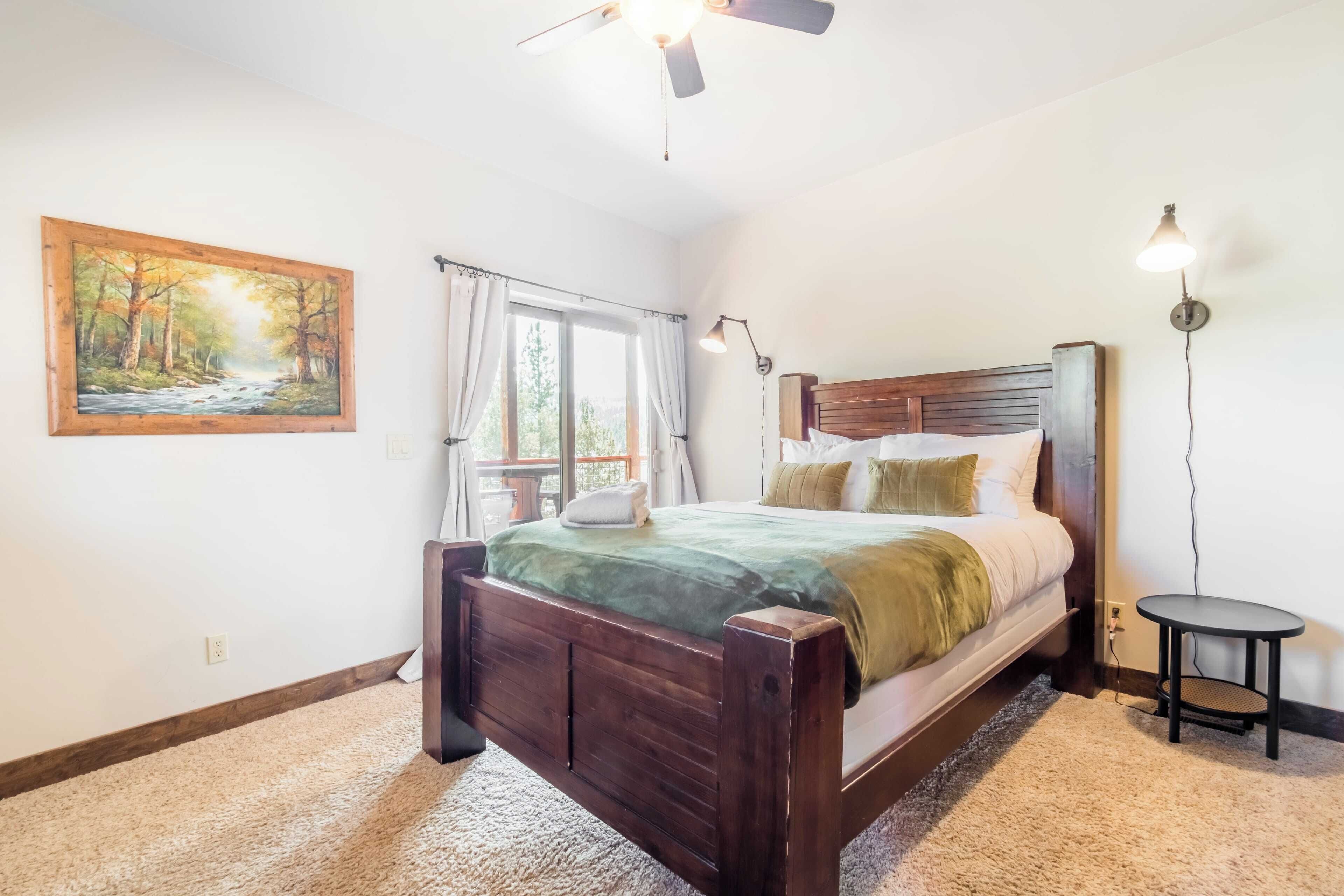 A bedroom with a wooden bed, a painting of a forest, a ceiling fan, a window with curtains, and a bedside table.