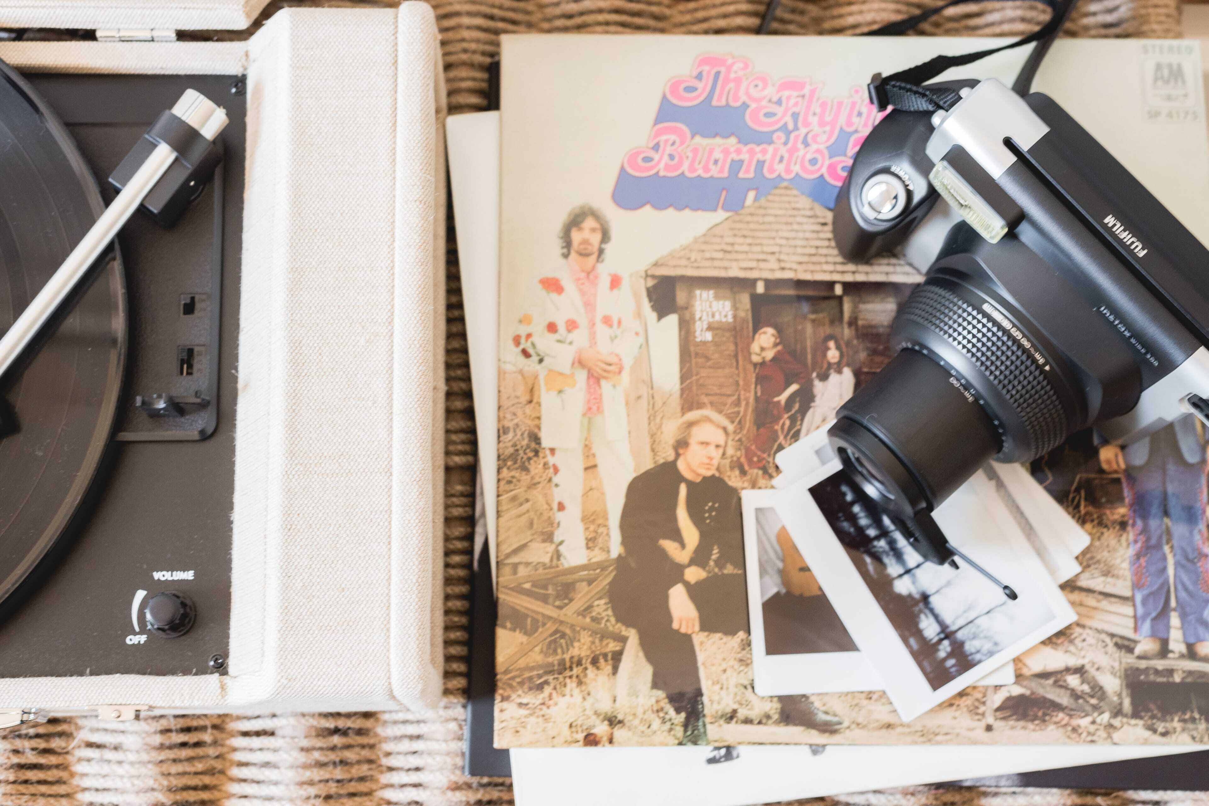 Una cámara Polaroid antigua, un tocadiscos de vinilo y un libro titulado 'The Flying Burrito Brothers'.