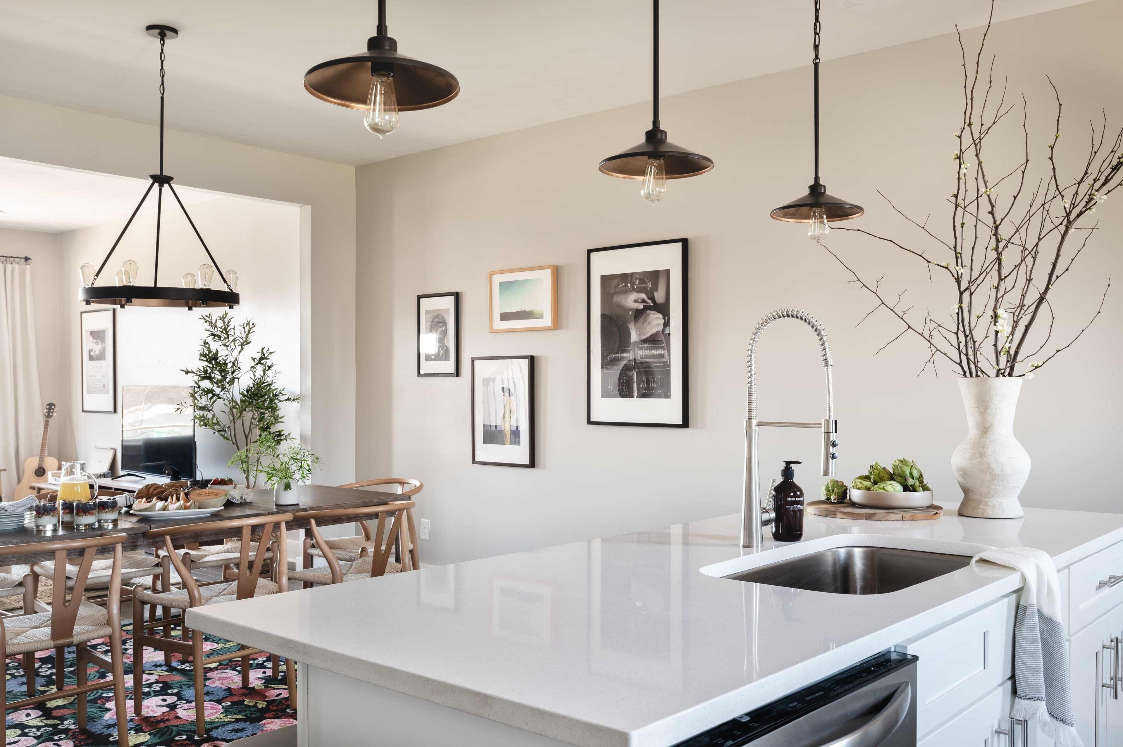 Een moderne keuken met een centraal eiland, hanglampen, ingelijste foto's aan de muur en een vaas met takken.