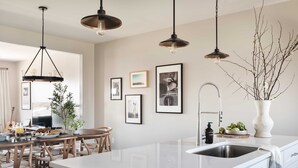 A modern kitchen with a central island, pendant lights, framed pictures on the wall, and a vase with branches. - Chesney by Avantstay Contemporary East Nashville Home w/ Southern Flare (Nashville)