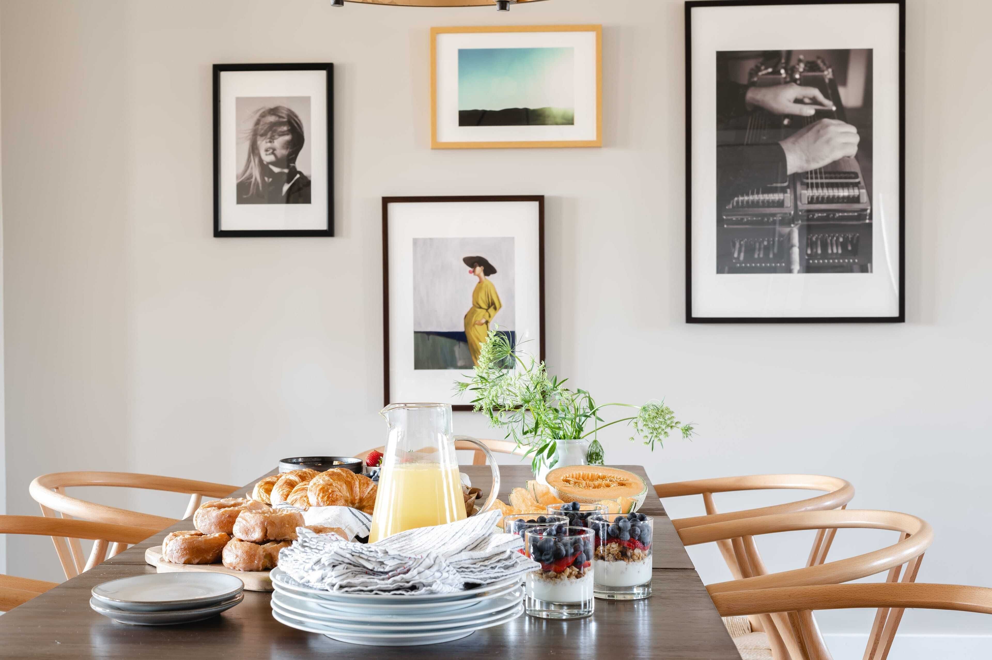 Une table de petit-déjeuner avec des viennoiseries, une carafe de jus d’orange et un journal.