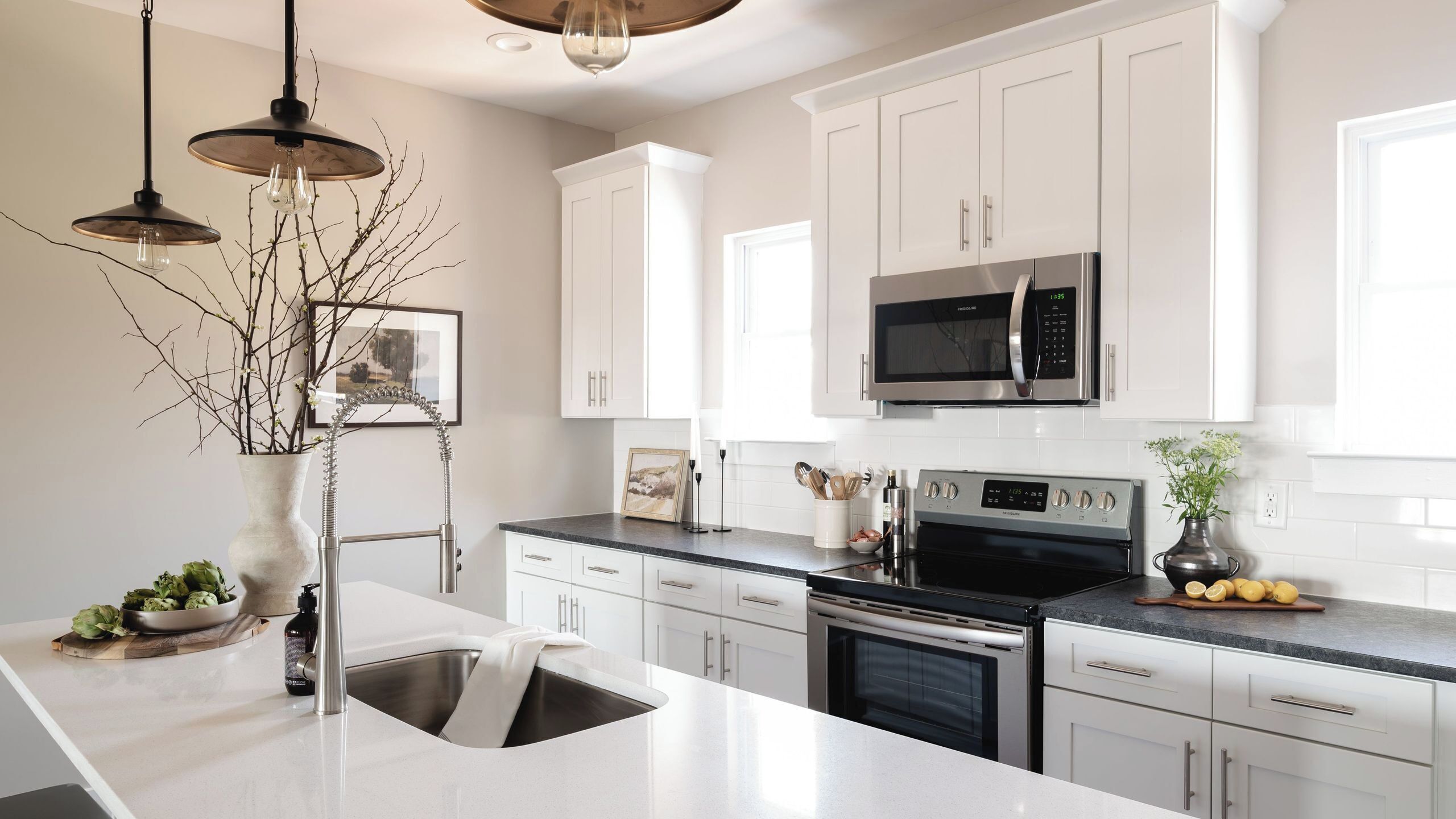 A modern kitchen with white cabinets, stainless steel appliances, and pendant lighting.