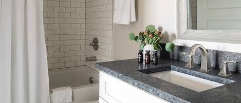 A bathroom with a white tiled shower, a white bathtub, a sink with a granite countertop, and a mirror above the sink.