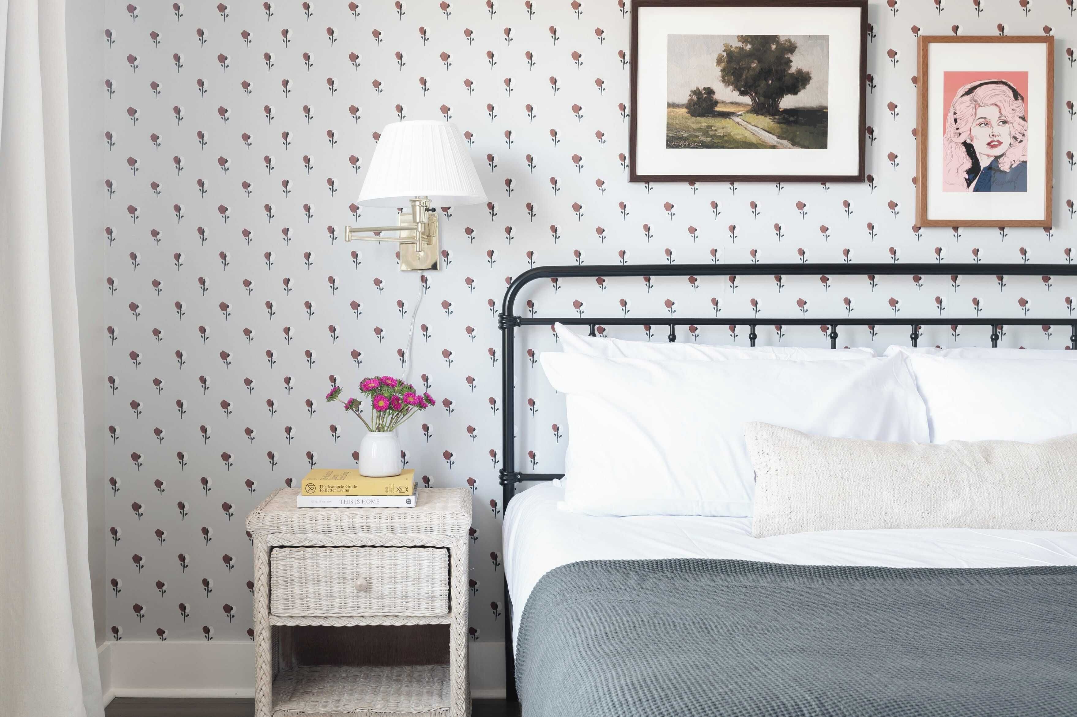 Un lit bien fait, avec du linge de lit blanc, une couverture grise et une petite table de chevet sur laquelle se trouvent une lampe et un vase de fleurs.