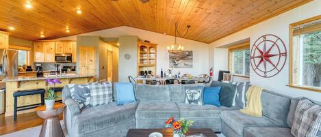 A spacious living area with a gray sectional sofa, a coffee table with a vase of flowers, and a wooden ceiling fan.