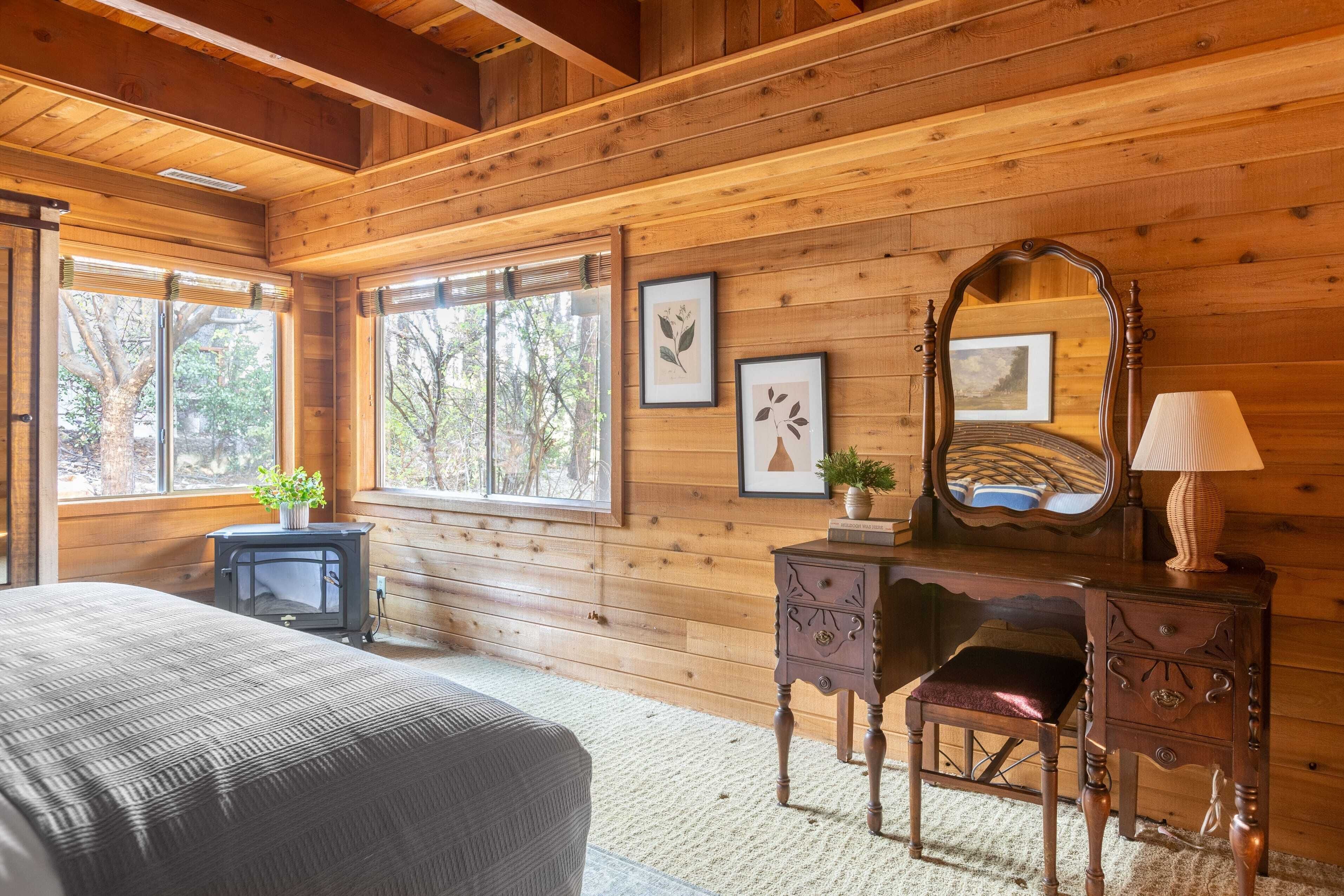 Acogedora habitación tipo cabaña con paredes de madera, una cama, un aparador, un espejo y cuadros enmarcados.