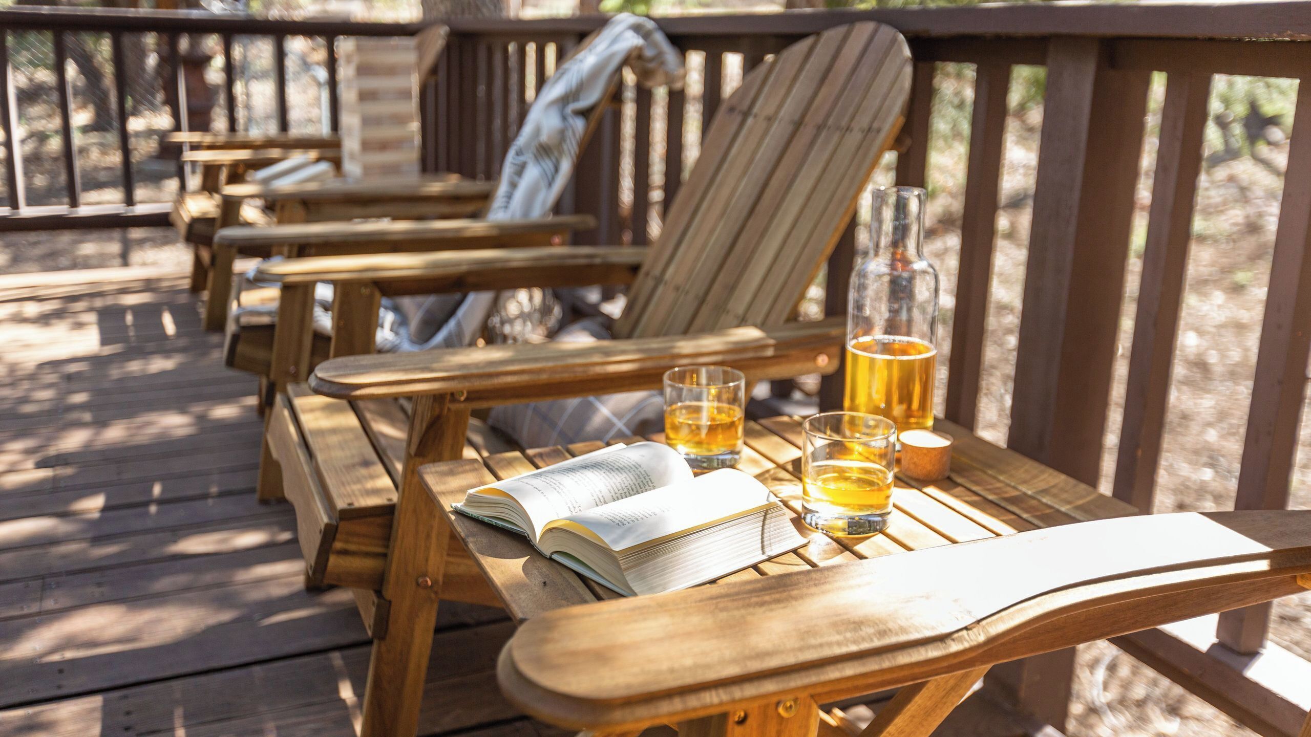 Een houten terras met enkele Adirondack-stoelen, een biertje en twee bierglazen.