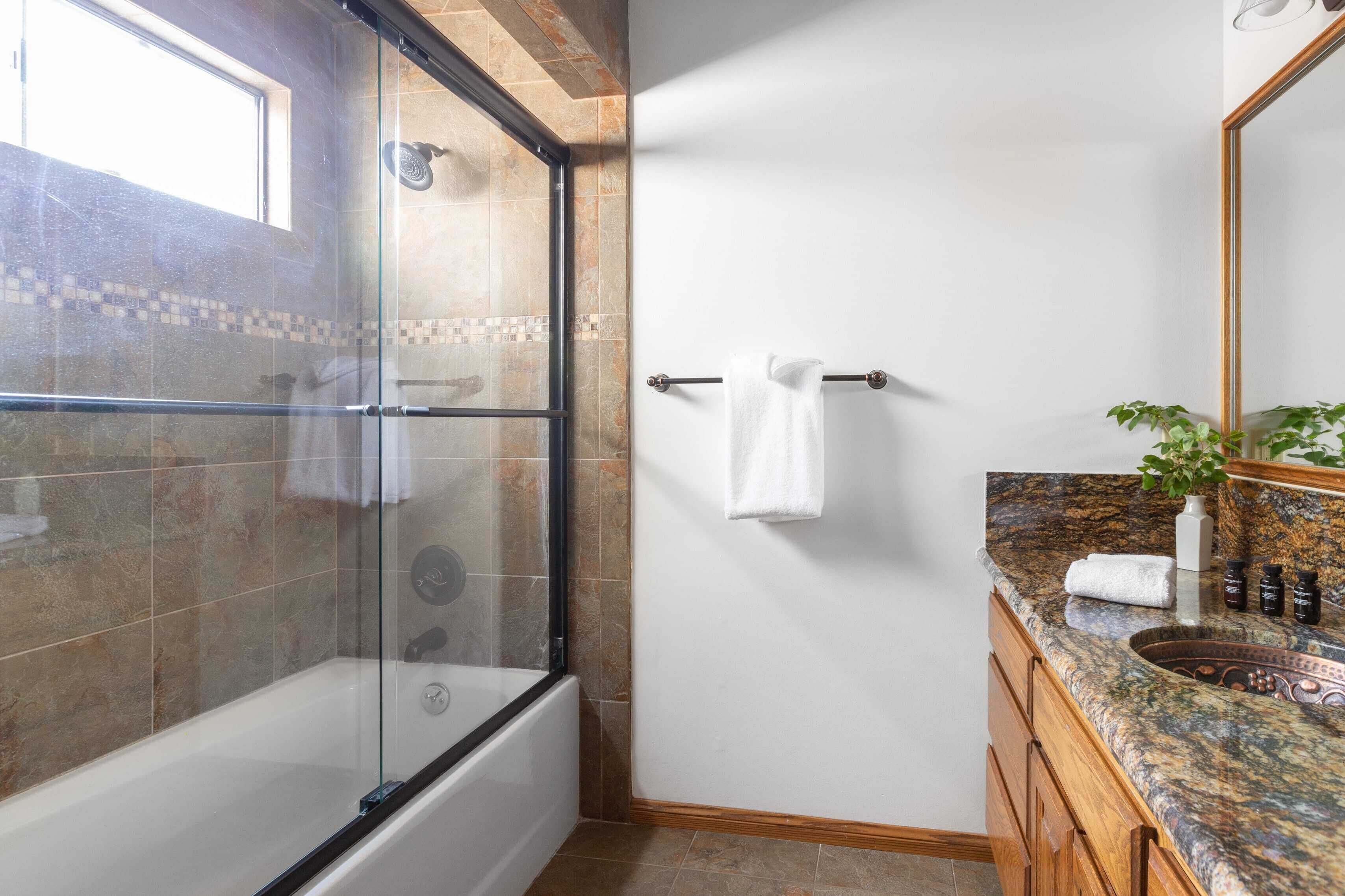 Un baño con ducha envuelta en vidrio, una bañera, tocador con encimera de granito y un espejo.
