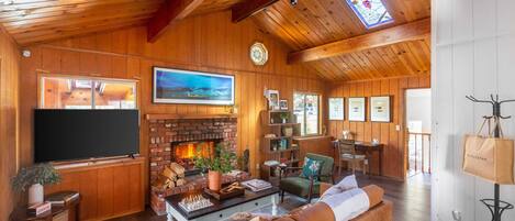 Una sala de estar acogedora con chimenea, paredes de madera, un televisor grande y un espacio de descanso confortable.