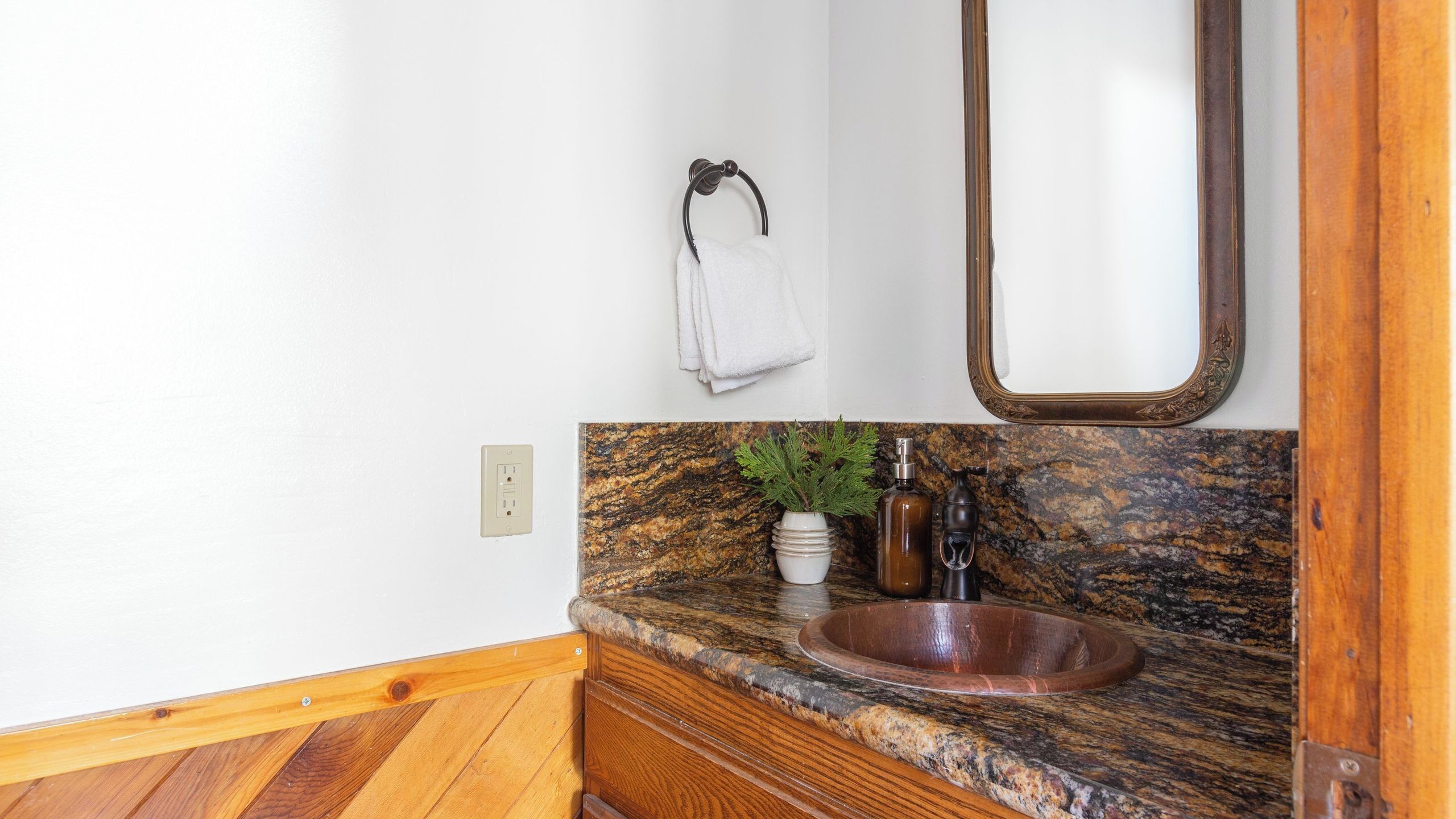 Une salle de bain avec un meuble-lavabo en bois, un plan de travail en granit, un lavabo en bois, un miroir, un porte-serviettes et une plante en pot.